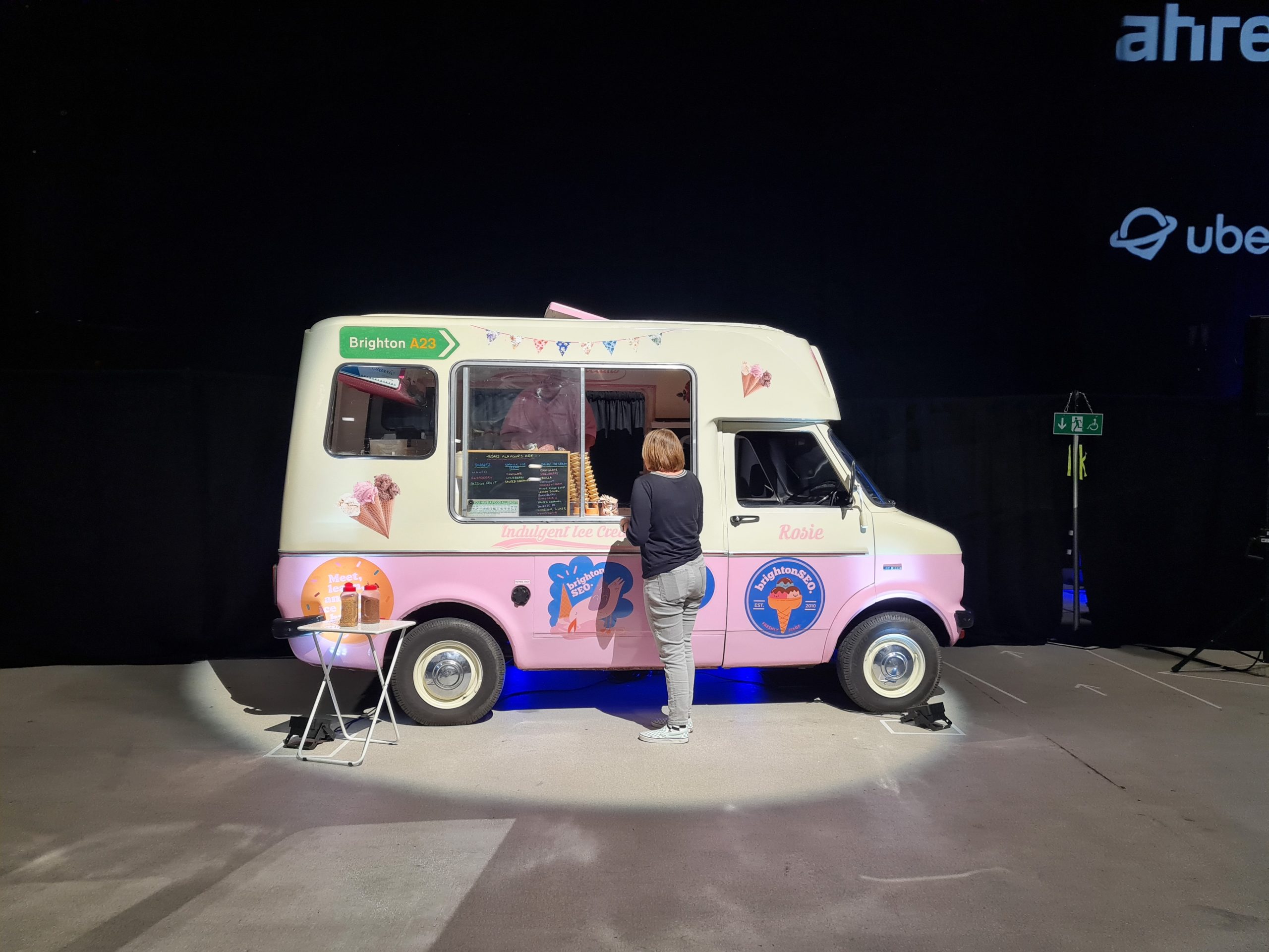 BrightonSEO - pink and white ice cream van in the corner of a large dark auditorium